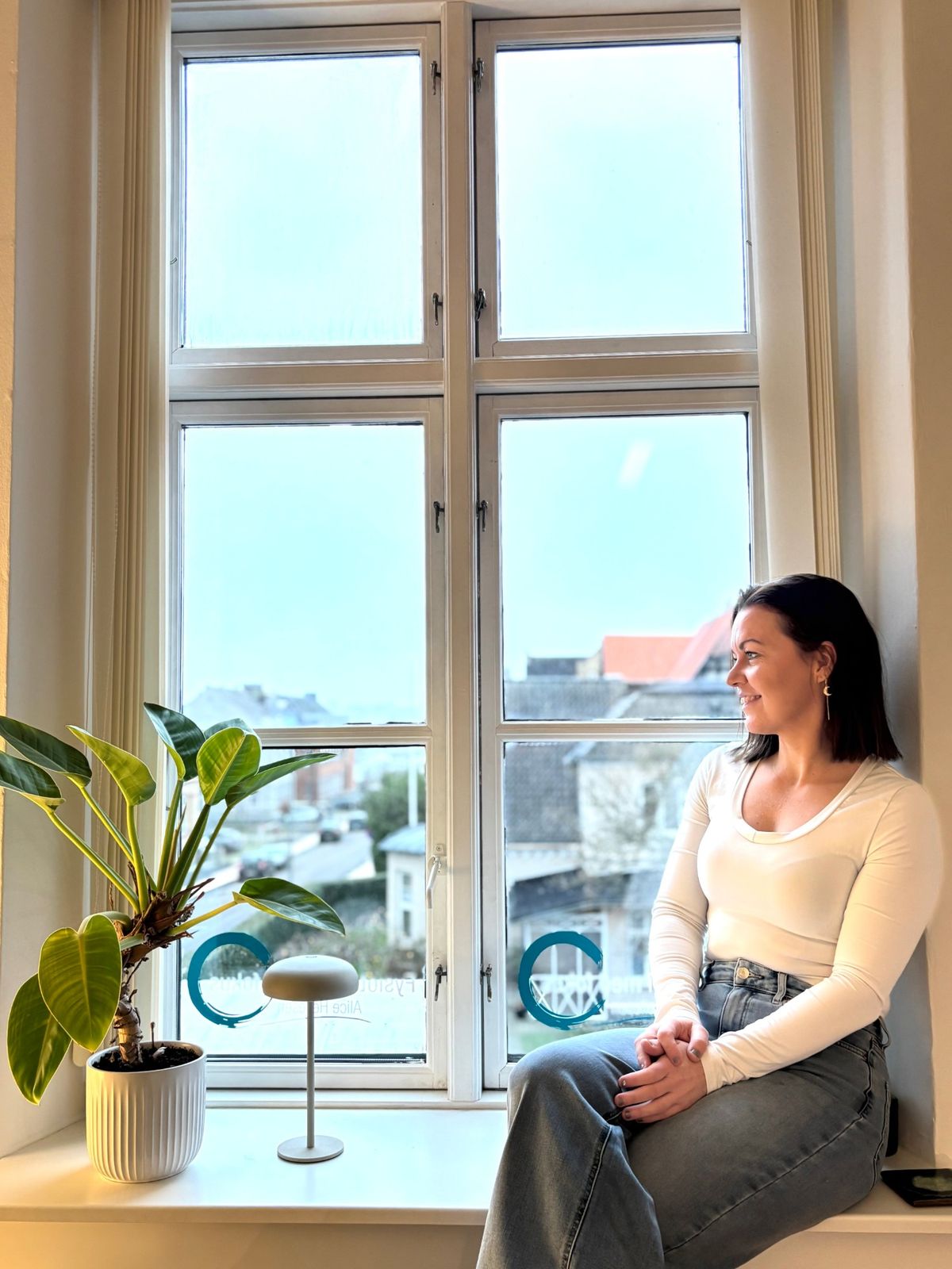 Alice Heilesen sidder i vindueskarmen i klinikken og kigger smilende ud over Sønderborgs tage
